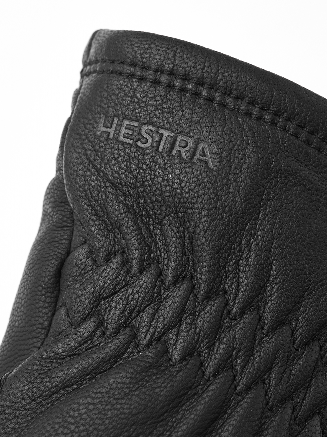 Close-up of a black leather glove with the lettering "HESTRA" and quilted accents.