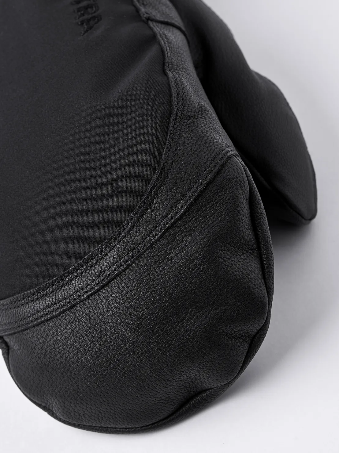 Gros plan sur une moufle noire Hestra Army Leather Extreme Mitt. Cuir sur la paume, textile sur le dos de la main.