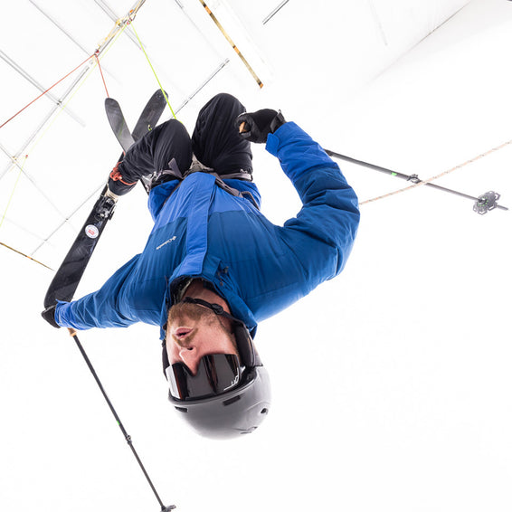 Un uomo con sci e bastoncini è appeso a testa in giù a delle corde e indossa occhiali da sole del tipo "The Synthesizer The Standard".