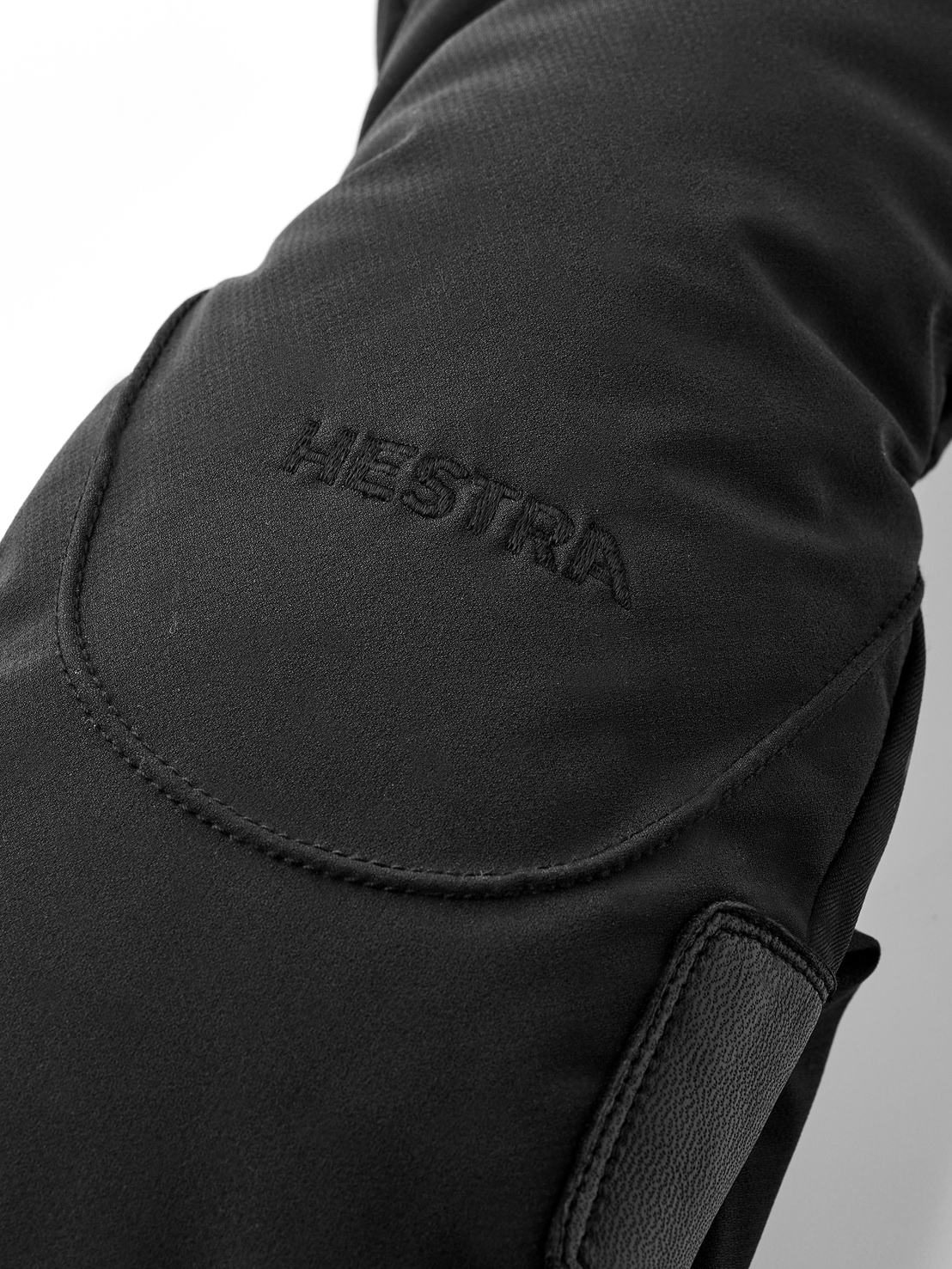 Détail d'un gant noir Hestra avec nom de la marque brodé et empiècements en cuir.