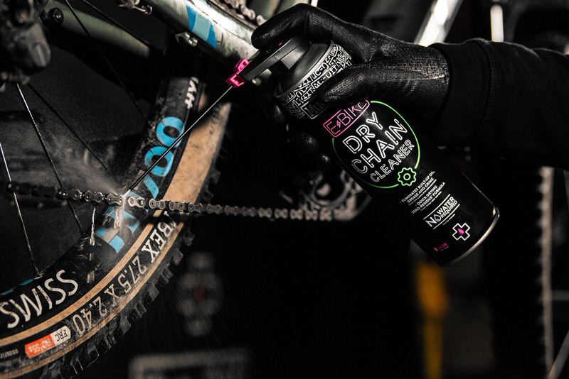 E-Bike Kettenpflege E-Bike Kettenreinigung: Eine Hand sprüht Dry Chain Cleaner auf eine Fahrradkette. Im Fokus: Sprühnebel und die Produktflasche.