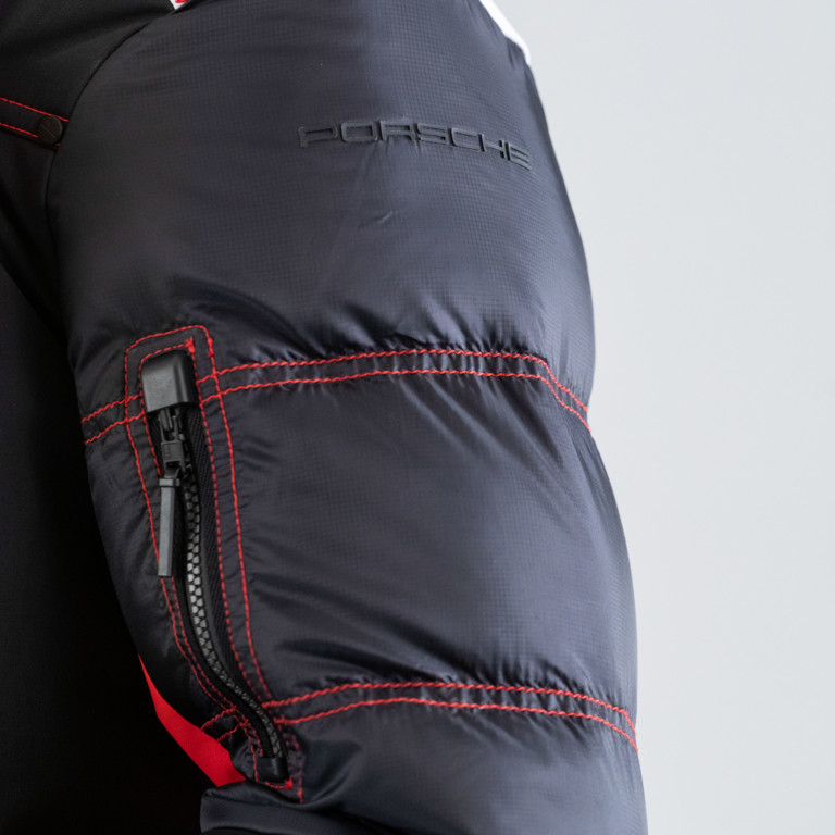 Détail de la manche d'une veste de ski PORSCHE noire avec couture rouge et fermeture éclair. Le logo PORSCHE est visible.