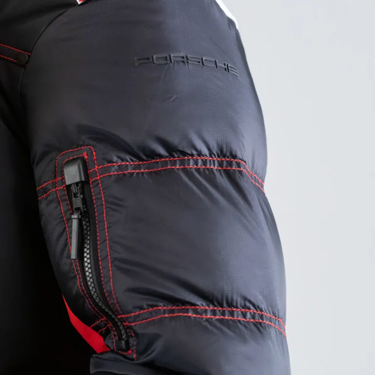 Particolare della manica di una giacca da sci PORSCHE nera con cuciture e zip rosse. Il logo PORSCHE è visibile.