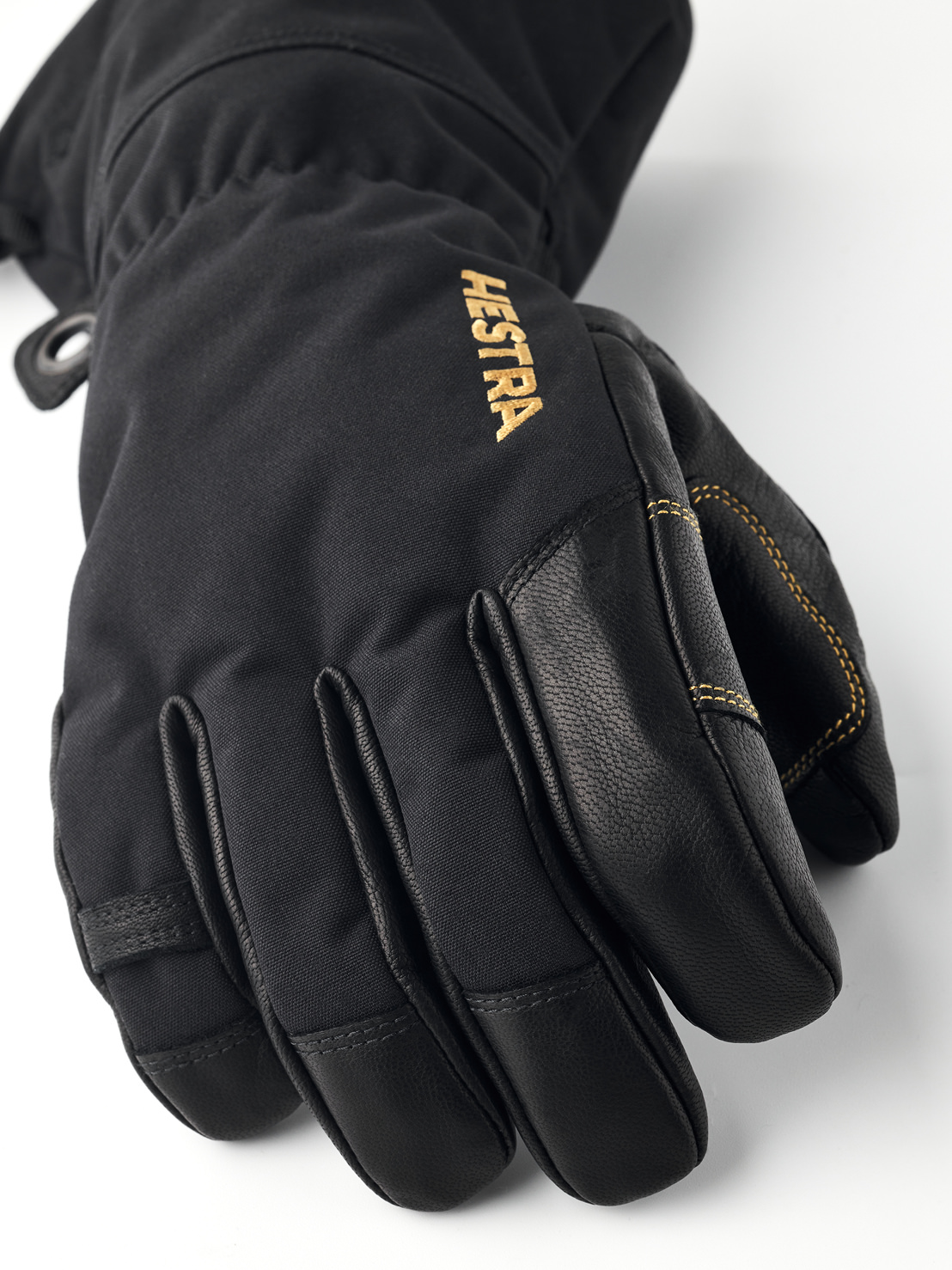 Black Hestra gloves Close-up of a black Hestra Gore-Tex five-finger glove with leather details and gold Hestra lettering.