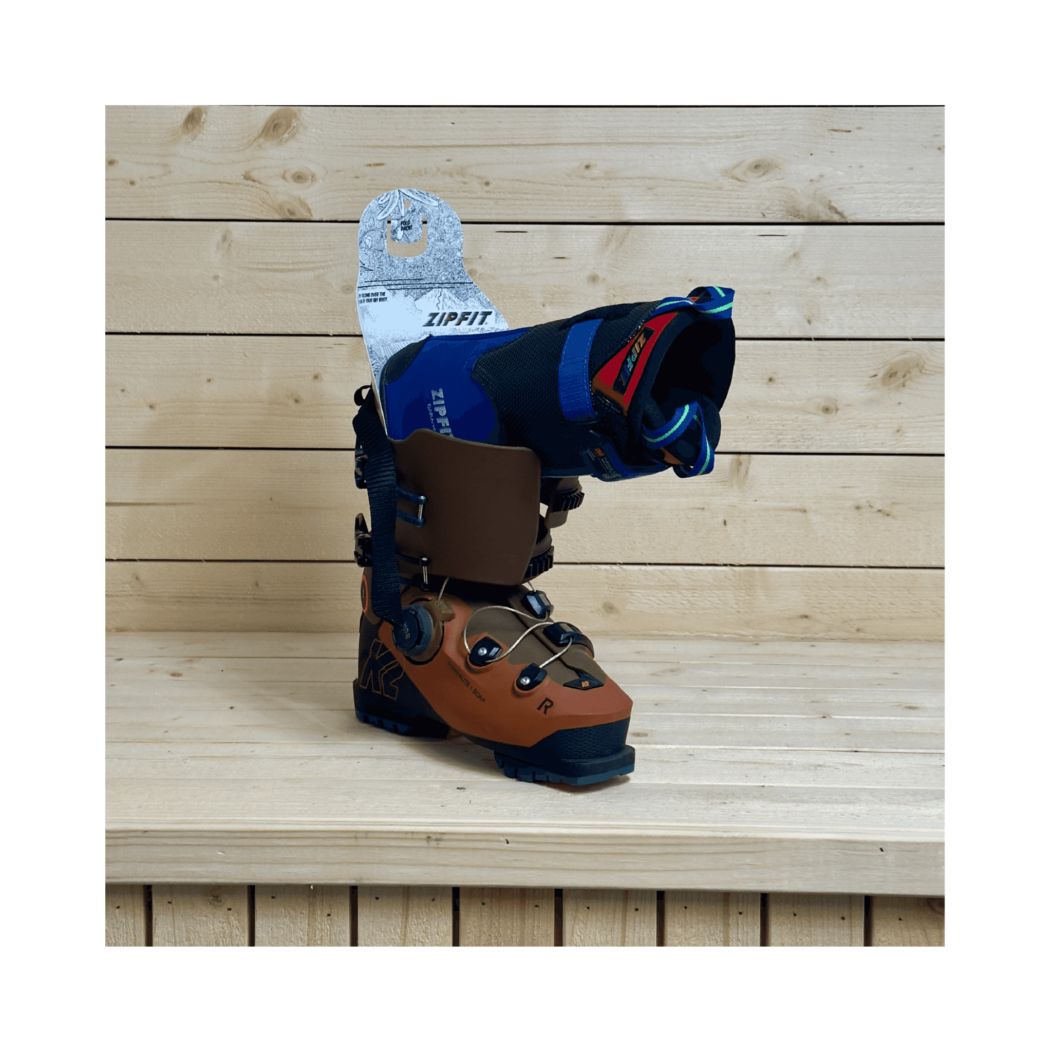 Uno scarpone da sci marrone con scarpone interno aperto si trova di fronte a una parete di legno. Lo scarpone interno è blu e nero con accenti colorati.