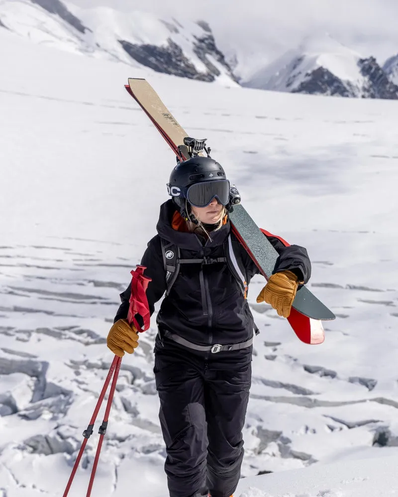 Person in schwarzer Gore-Tex Jacke und Skihose mit Skiern und Stöcken in verschneiter Berglandschaft.
