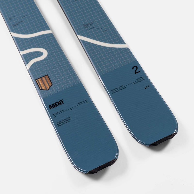 Zwei blaue Ski liegen nebeneinander, mit weißen Akzenten, Rastermuster und Textdetails. Details zu Material und Design sind aufgedruckt.