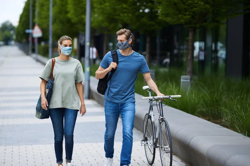 Deux personnes portant des masques, l'une avec un marakrana bleu clair Sky Blue, se promènent, l'homme avec un vélo.