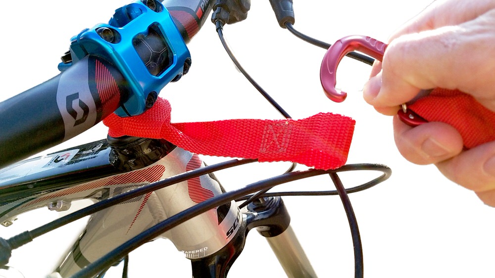 Nahaufnahme: Tow-Whee Quick Loop-Befestigung am Fahrradlenker, Karabinerhaken in der Hand. Rote Schlaufe.