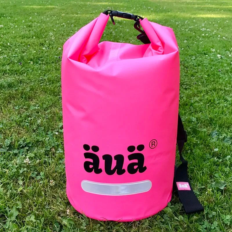 Pinker Dry Bag mit Tragegriff und Schultergurt auf grünem Gras. Das Logo "äua" ist aufgedruckt.