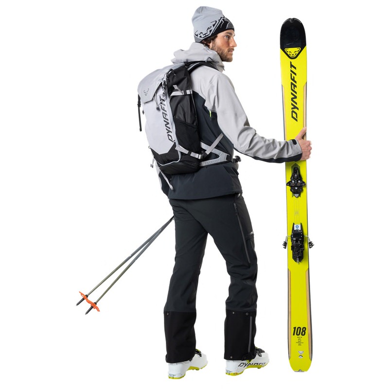 Ein Mann mit Dynafit Beast Hybrid Jacke, Skiern, Rucksack und Skistöcken.