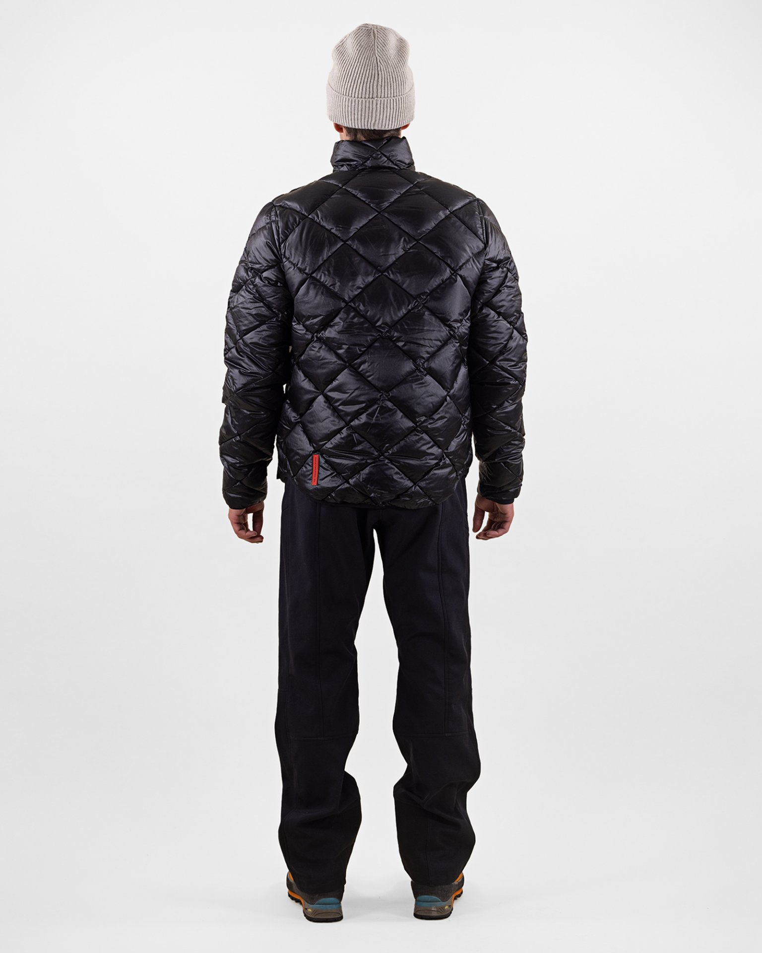 Doudoune noire Personne de dos, portant une doudoune noire à losanges, un pantalon et une casquette.