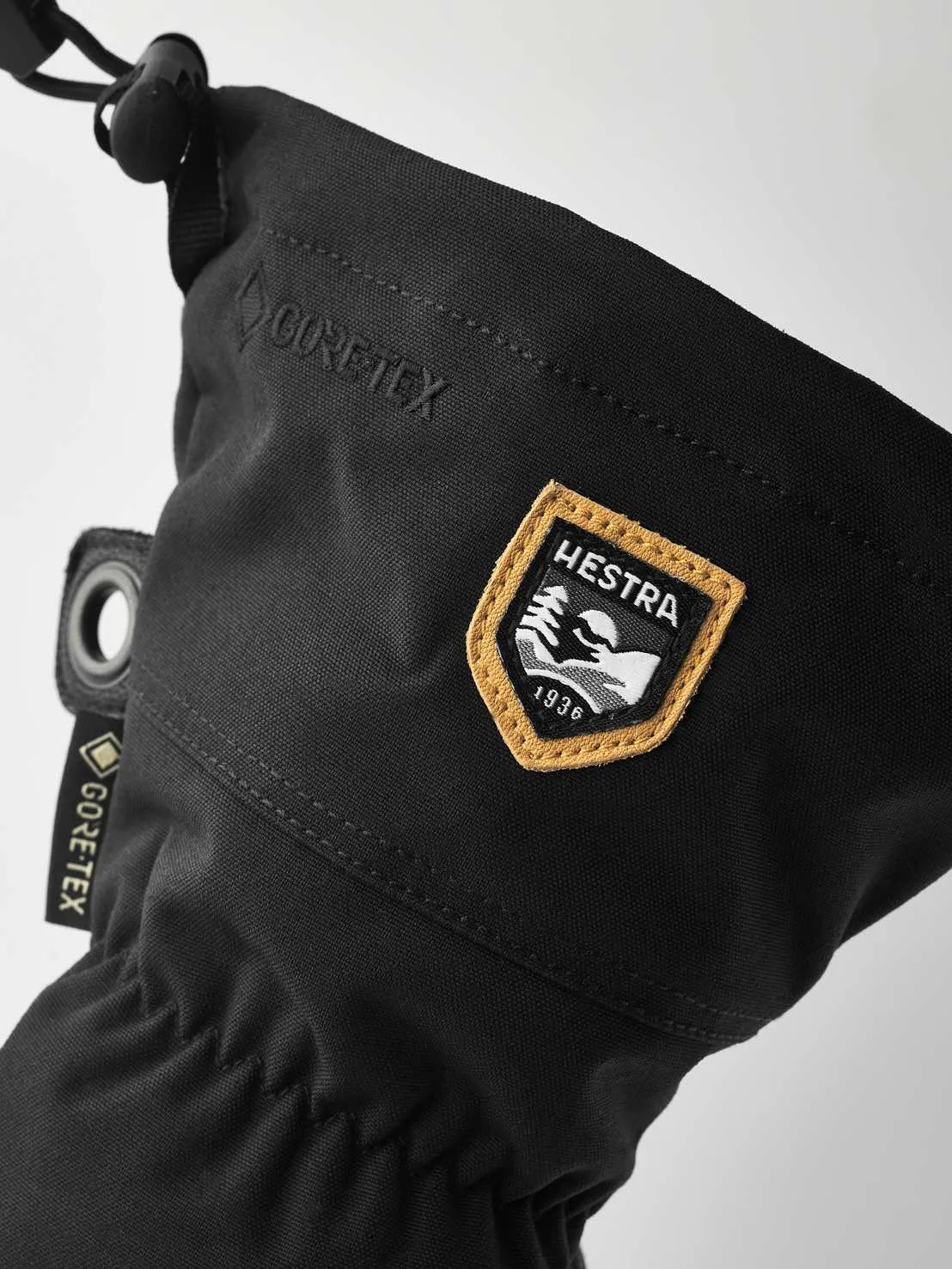 Close-up of a black Hestra Army Leather Gore-Tex mitten with logos and drawstring.
