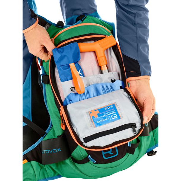 Geöffneter Free Rider 24 Rucksack in Grün/Schwarz mit Lawinenschutzausrüstung und Notfallkarte.