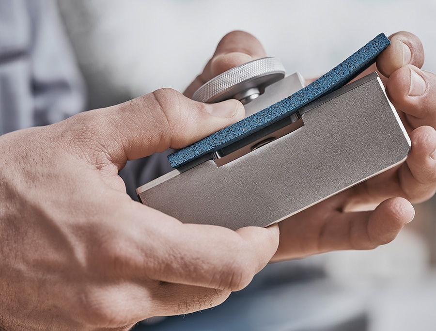 Hände halten ein Werkzeug mit blauem Polierblock und silbernem Einstellrad.