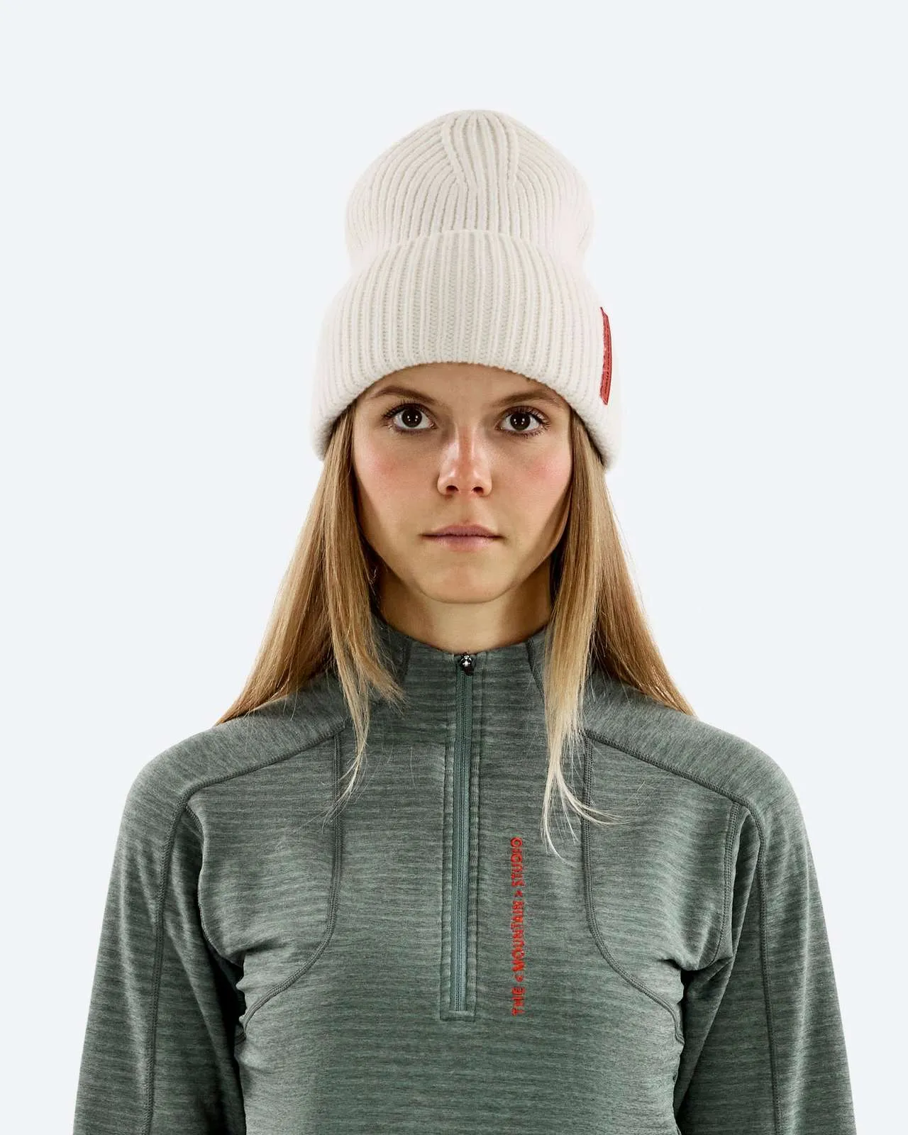 Ritratto di donna con capelli biondi che indossa un berretto bianco e un top verde con cerniera.