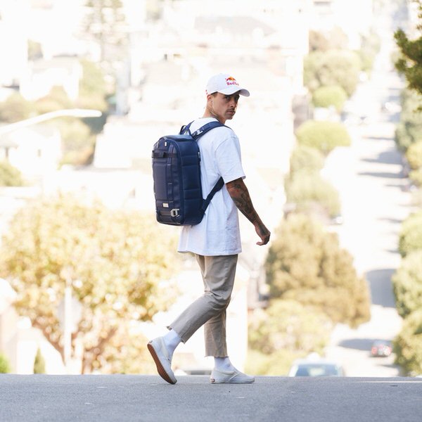 Mann mit blauem Douchebags The Backpack Leder, seitliche Träger, geht auf einer Straße.