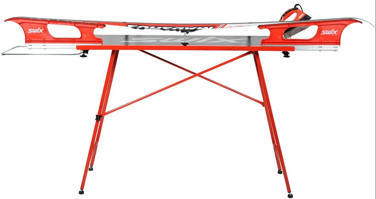 Table de fartage rouge pour skis de Swix avec skis et fer à repasser. Table réglable en hauteur, pieds antidérapants.