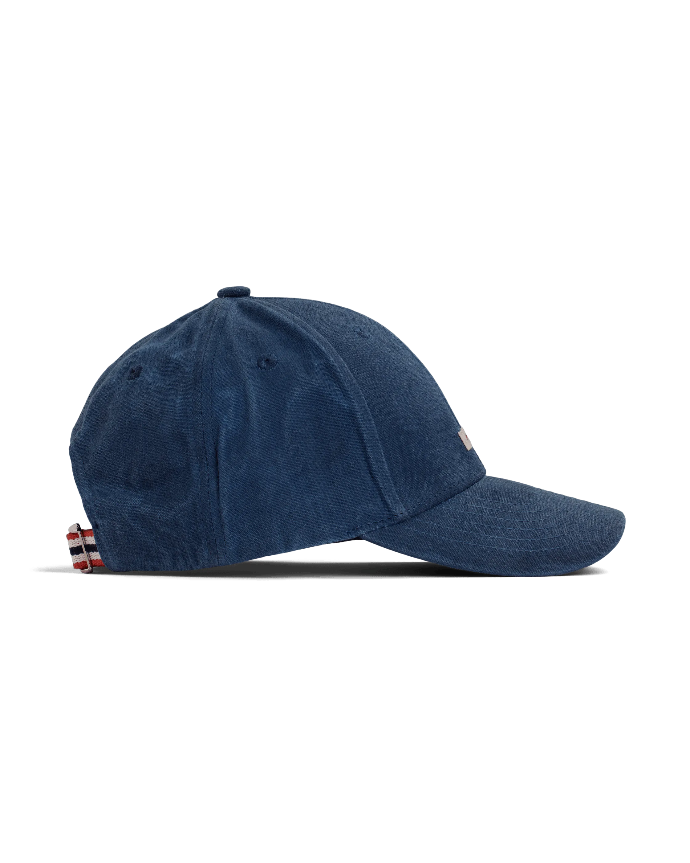 Vista laterale di un cappellino in cotone cerato blu navy linea "Amundsen" su sfondo bianco. Con bottone sulla sommità, visiera ricurva e laccio a righe rosse, bianche e blu sul retro per regolare la misura.