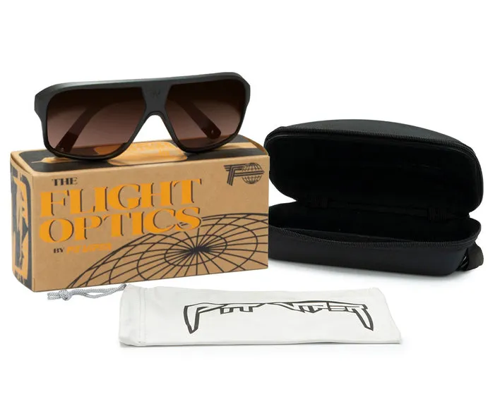 Occhiali da sole Flight Optics marrone scuro su scatola marrone. Custodia nera aperta, sacchetto bianco sotto.