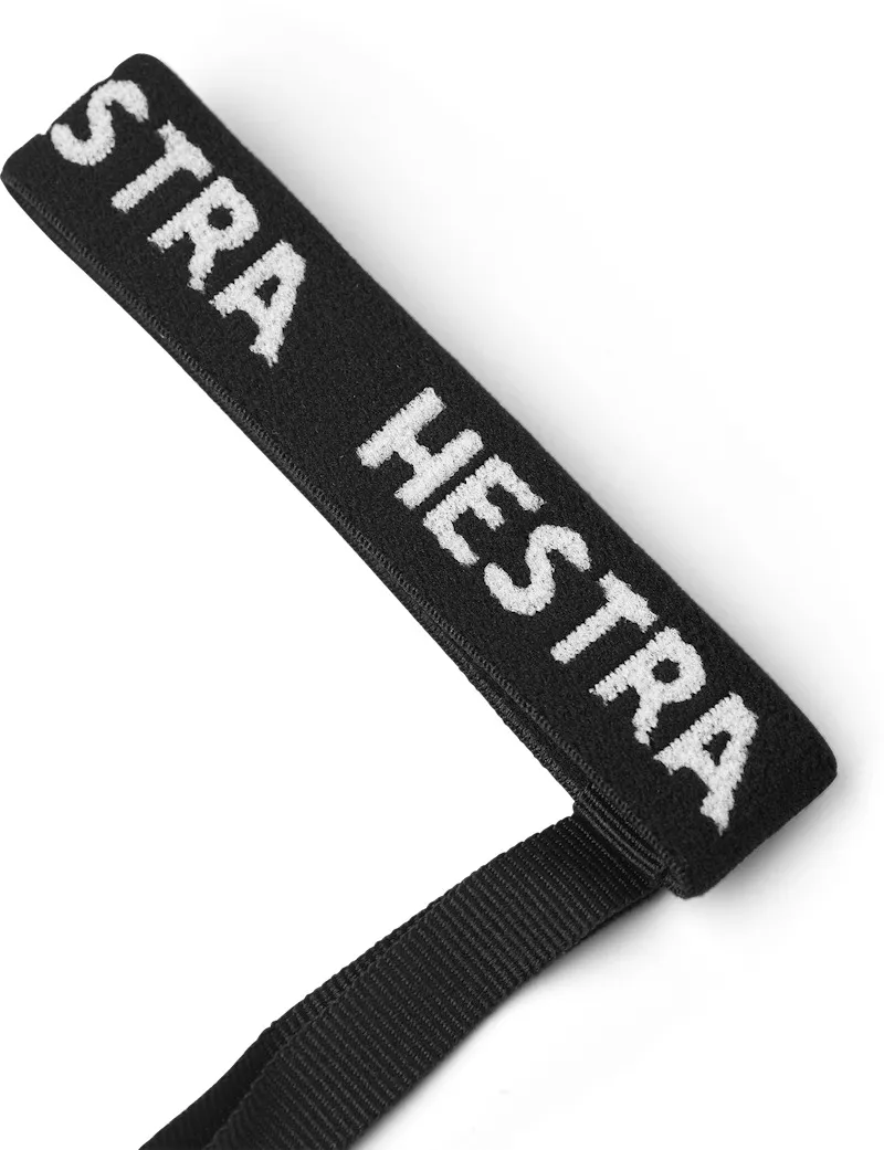Schwarzes Textilband mit weißem "STRA HESTRA" Schriftzug und schwarzem Band an einem Ende, auf weißem Grund.