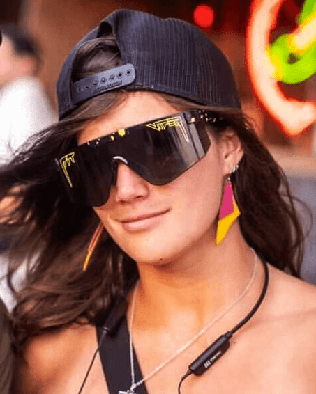 Look stylé avec néon Personne portant des lunettes de soleil "The Cosmos 2000", une casquette noire, une boucle d'oreille et des accents néon.