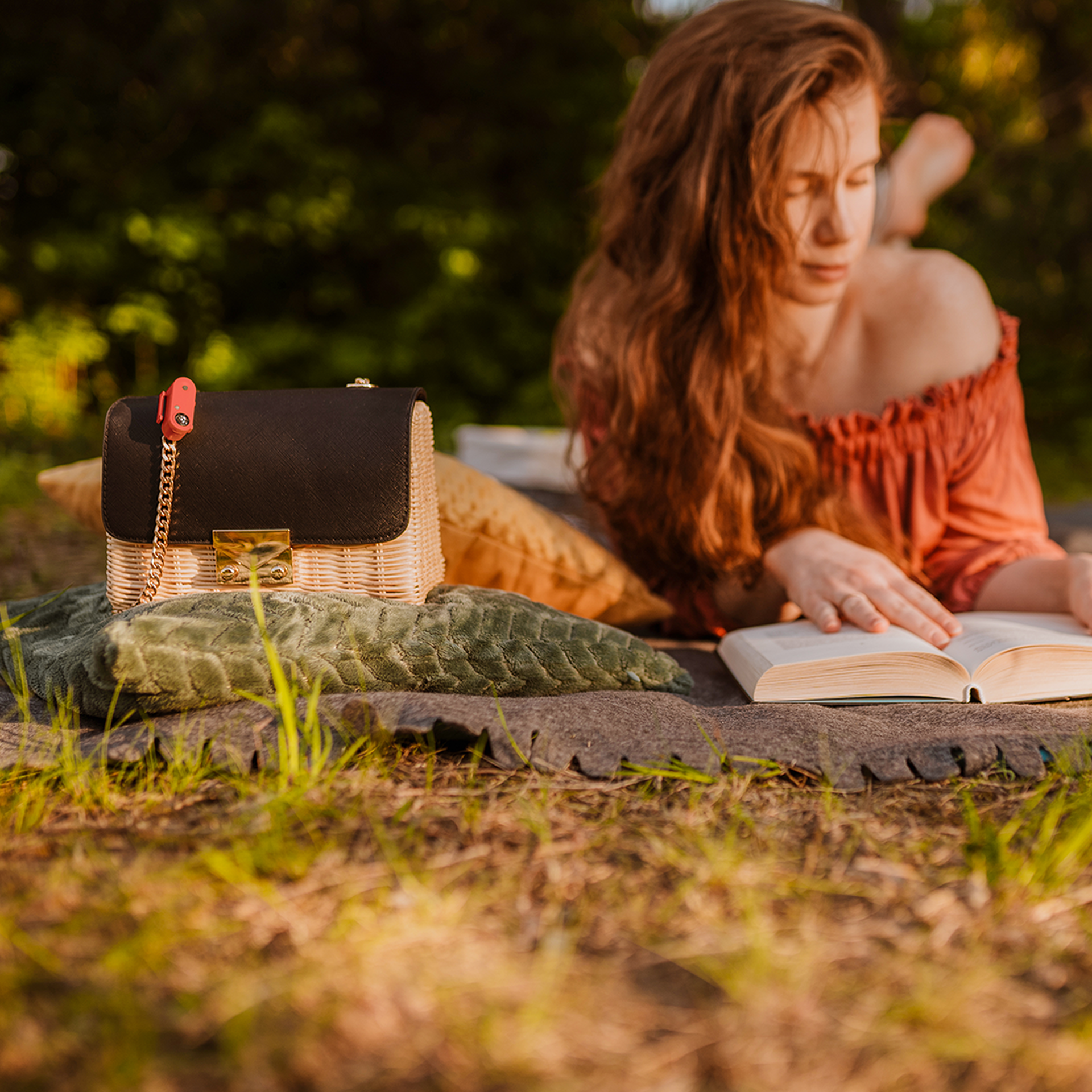 Frau beim Picknick Draufsicht: Frau liest Buch auf Picknickdecke im Freien, Tickless Active am Korb mit Tasche befestigt.