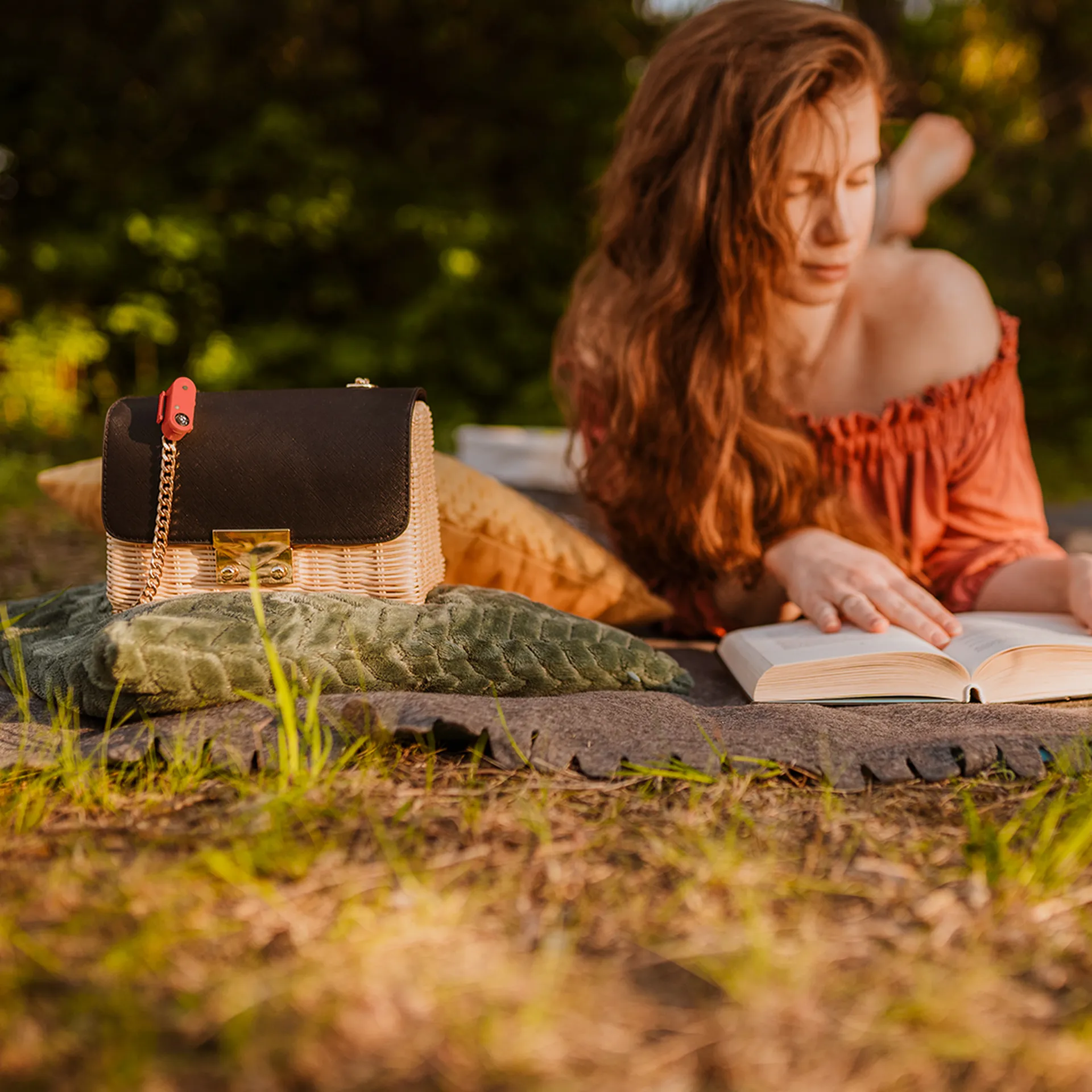 Vista dall'alto: donna che legge un libro su una coperta da picnic all'aperto, Tickless Active attaccato a un cestino con borsa.