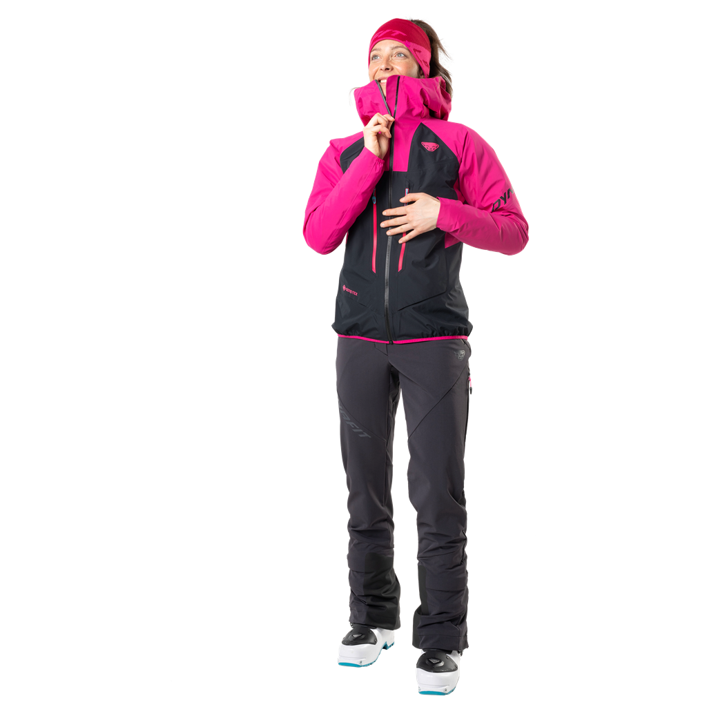 Femme en pantalon Dynafit TLT Touring DST, noir, veste rose, chaussures de ski, vue vers le haut.