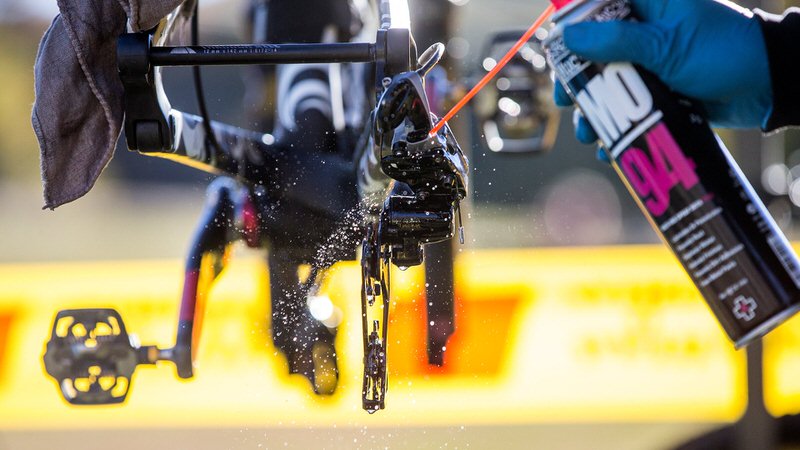 Ein Fahrrad wird mit Muc-Off MO-94 Spray behandelt. Nahaufnahme der Fahrradkette und des Sprays, Fokus auf Schmierung und Schutz.