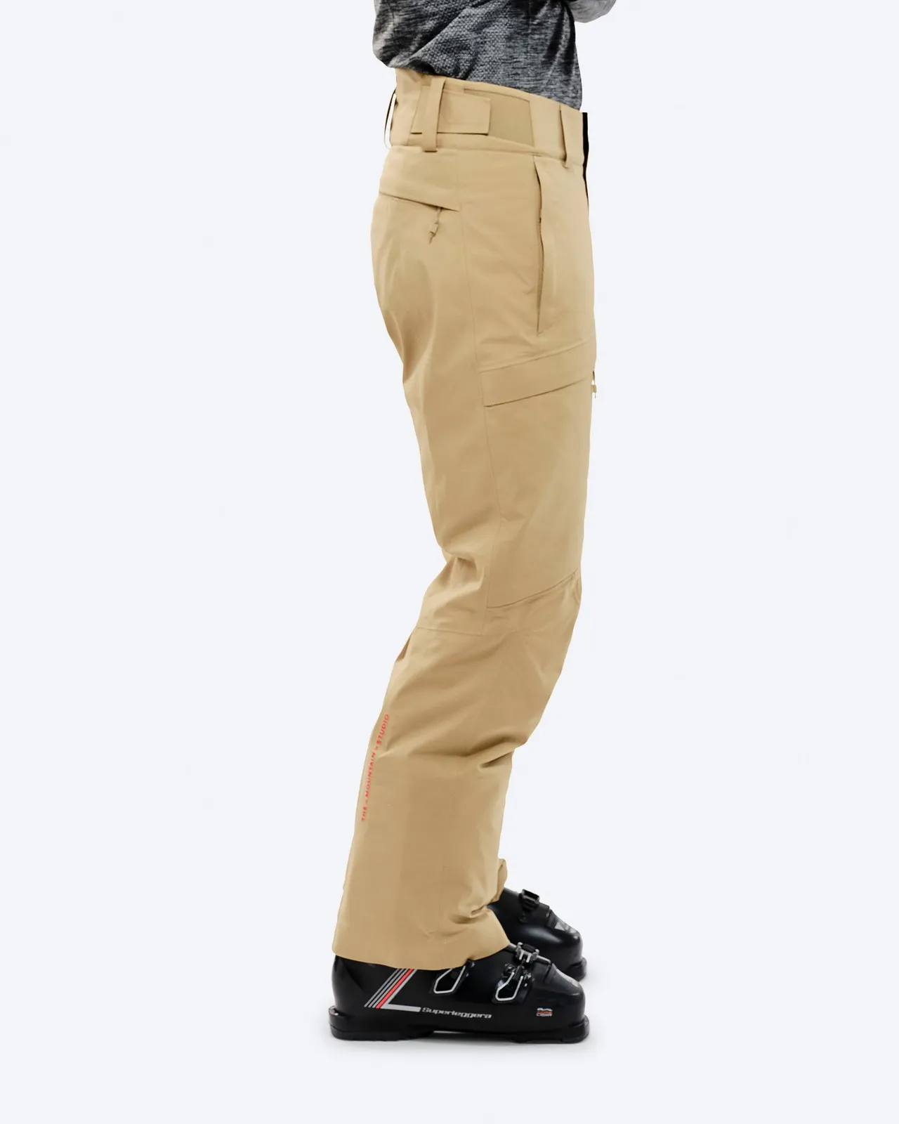 Sand-colored GORE-TEX 2L stretch ski pants on the body with ski boots, side view.