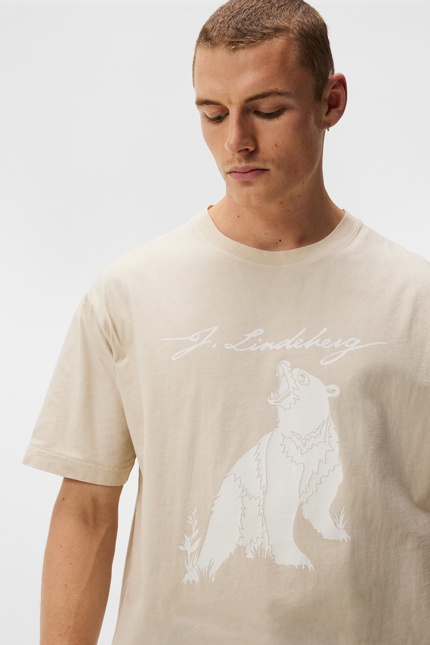Tee Walsh Boxy Print Un modèle porte le tee-shirt Walsh Boxy Print en Oyster Gray avec un imprimé ours blanc et une inscription J.Lindeberg.
