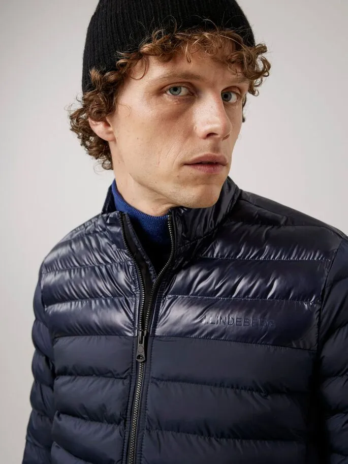 Uomo con berretto che indossa una giacca Rick Light blu imbottita con cerniera e piccola scritta J.Lindeberg.