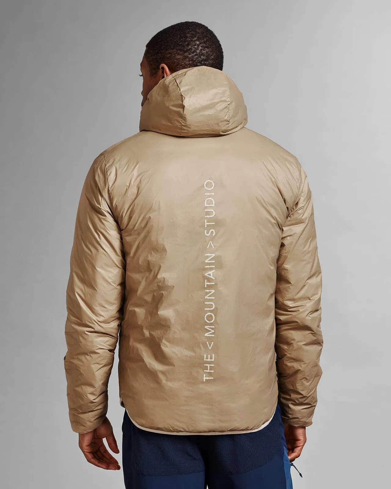 Back view of a beige D-3L Reversible Light Hood Jacket with hood, printed with "THESTUDIO".