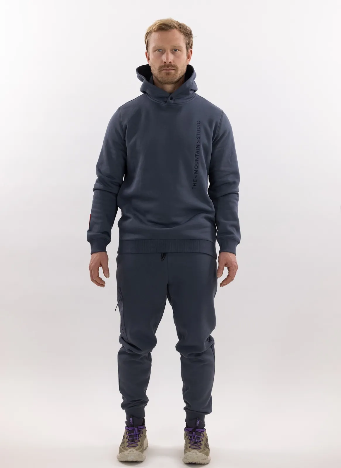 Man in gray Z-5 3L Hybrid Shell Jacket and matching pants from The Mountain Studio against a white background.