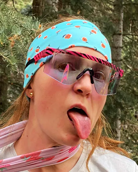 Donna con occhiali fotocromatici e fascia per capelli tira fuori la lingua.