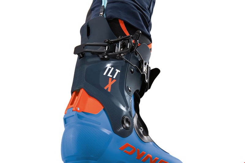 Nahaufnahme vom Dynafit TLT X Boot. Der Ski-Tourenschuh ist blau mit orangefarbenen Akzenten und hat einen schwarzen Verschluss.