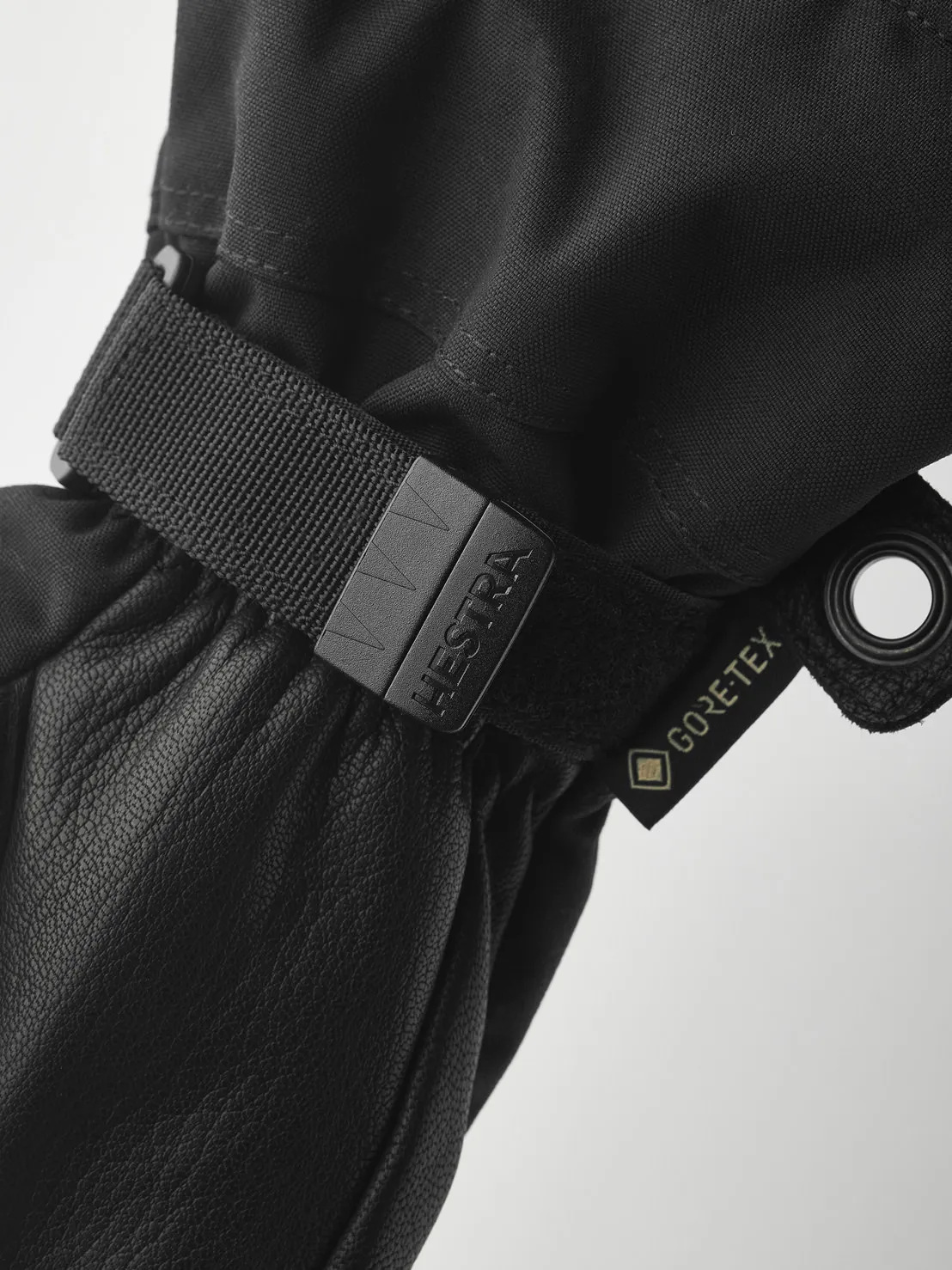 Gros plan sur un gant noir Hestra avec une étiquette Gore-Tex et une lanière réglable. Le matériau est du cuir et du textile.