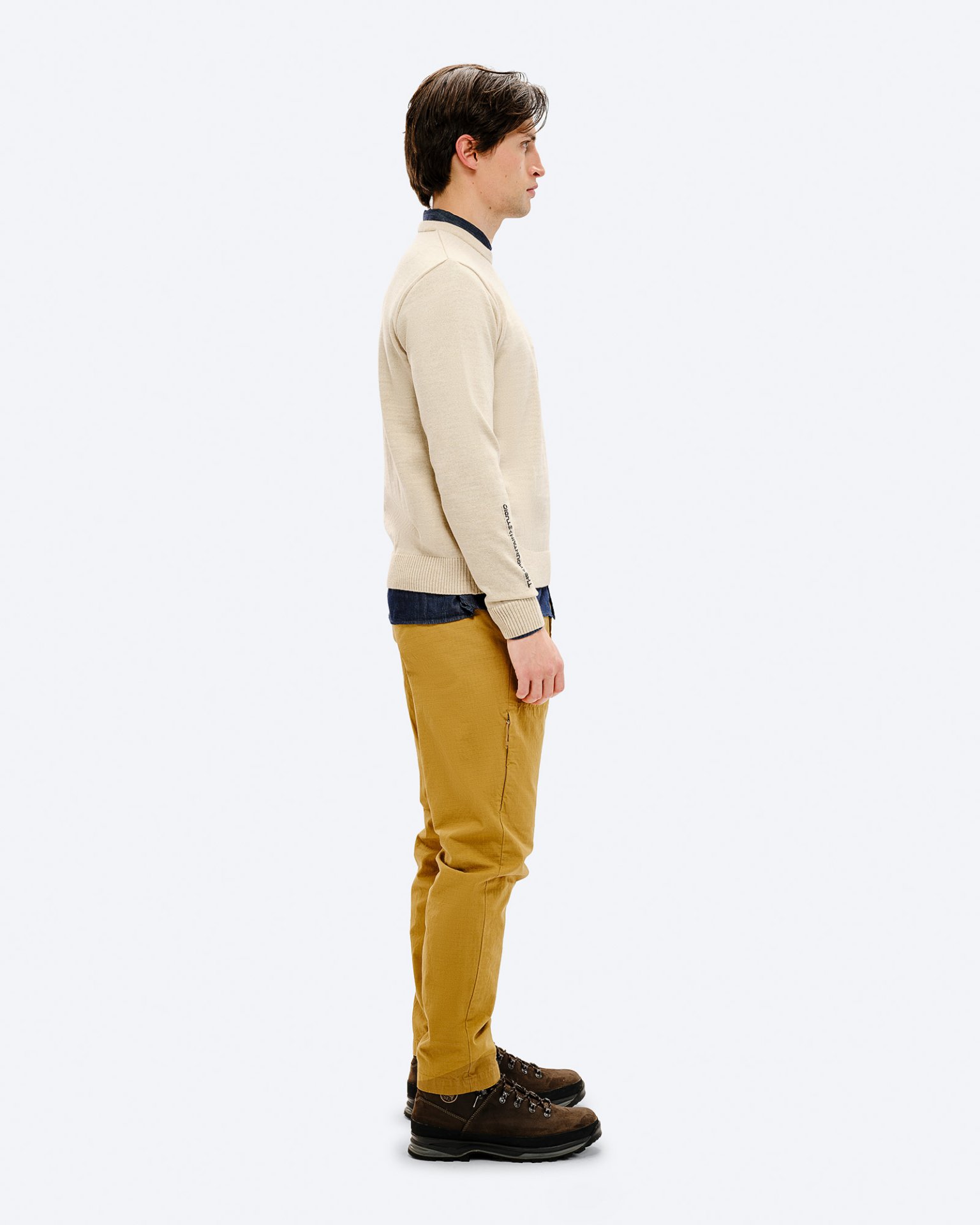 Man in the K-3 ST ski sweater A man, from the side, wearing the K-3 ST Ski Sweater in beige, combined with brown hiking boots and yellow pants.