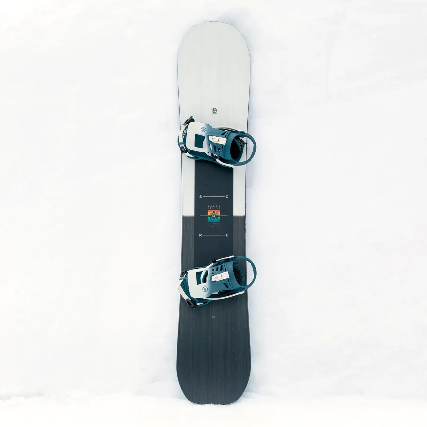 Das Nidecker Score Snowboard mit montierten Bindungen auf weißem Schnee. Das Board hat eine geteilte Farbgebung.