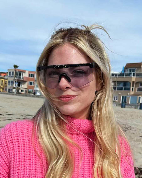 Blonde Frau mit pinkem Pullover und Cosmos Photochromic 2000 Sonnenbrille am Strand.