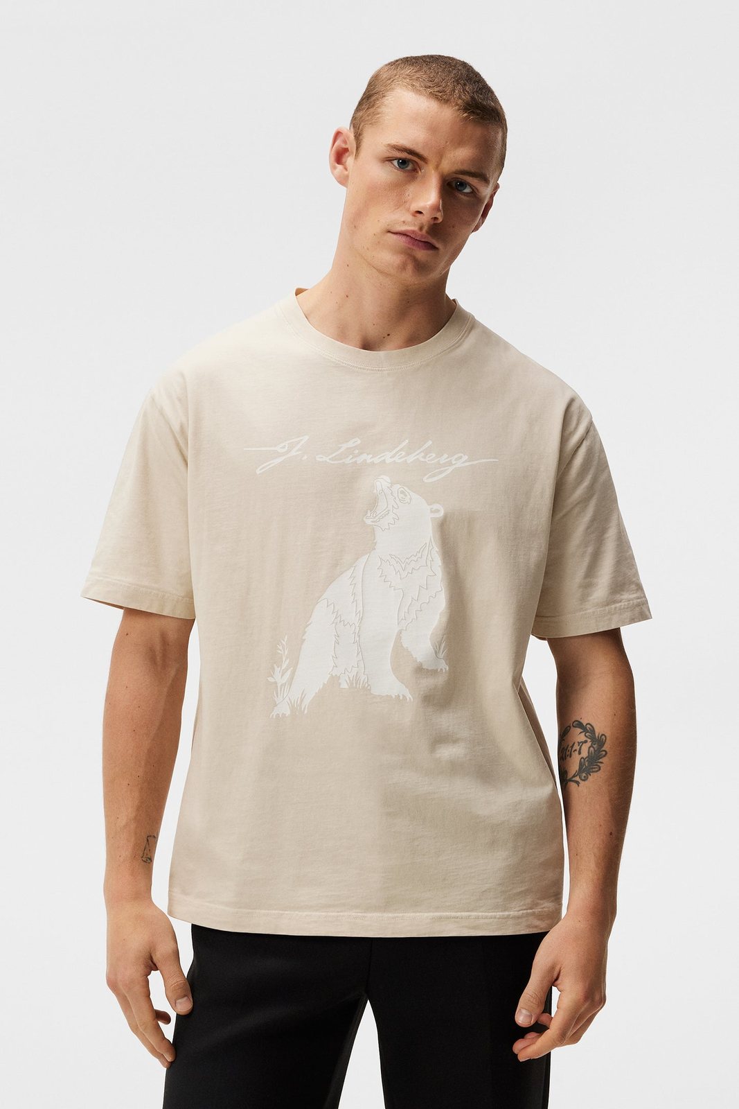 Model wears Walsh Boxy Print Tee Oyster Gray with bear motif and J.Lindeberg lettering.