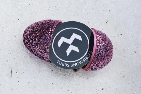Un paio di racchette da neve rosa scintillanti, legate insieme, con etichetta Tubbs Schneeschuhe, su neve bianca.