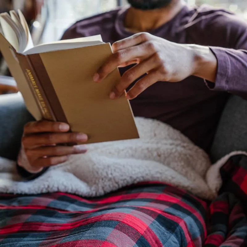Homme lisant un livre sous Buffalo Plaid Flannel Sherpa Blanket.