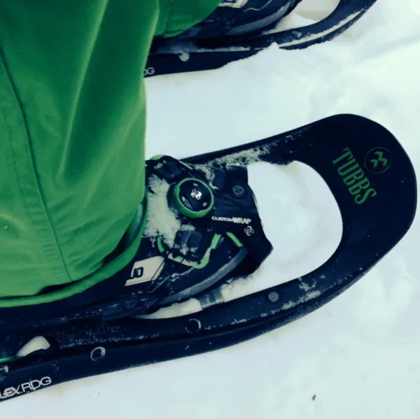 Primo piano delle racchette da neve Tubbs nella neve con una persona vestita di verde.