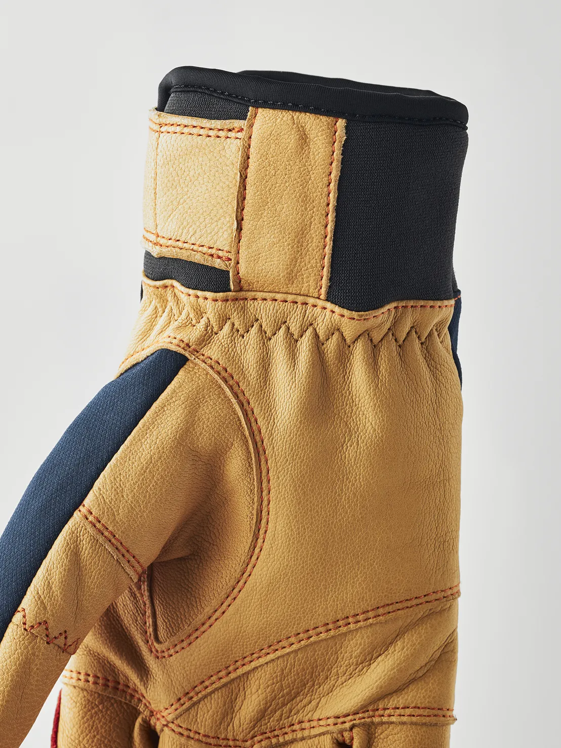 Gros plan sur un gant en cuir marron clair avec des accents bleus et des surpiqûres rouges, ainsi qu'une ceinture noire.