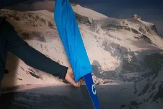 Close-up: Hand pulls blue ski skin stocking over ski skin, mountain scenery in the background.