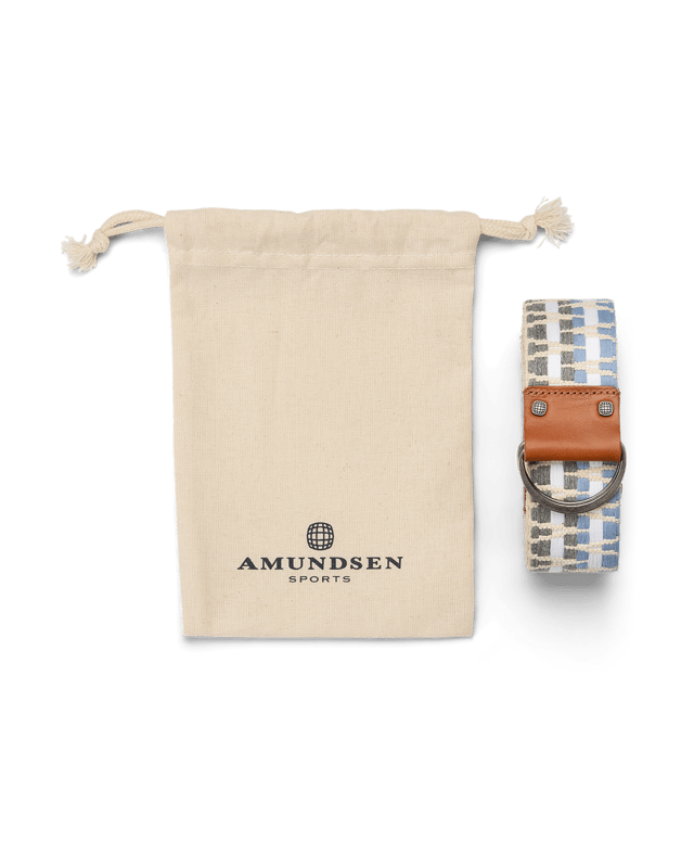 Beiger Baumwollbeutel mit Logo und karierter Gürtel mit Lederdetails und Metallring auf weißem Grund.