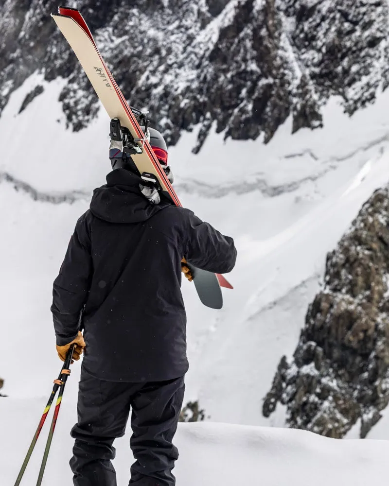 Person mit Skiern und Stöcken vor verschneitem Berg, trägt schwarze S-1 Gore Tex Jacke.