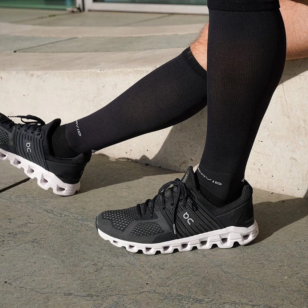 Legs with black MCDavid compression socks and sneakers on a stone staircase.